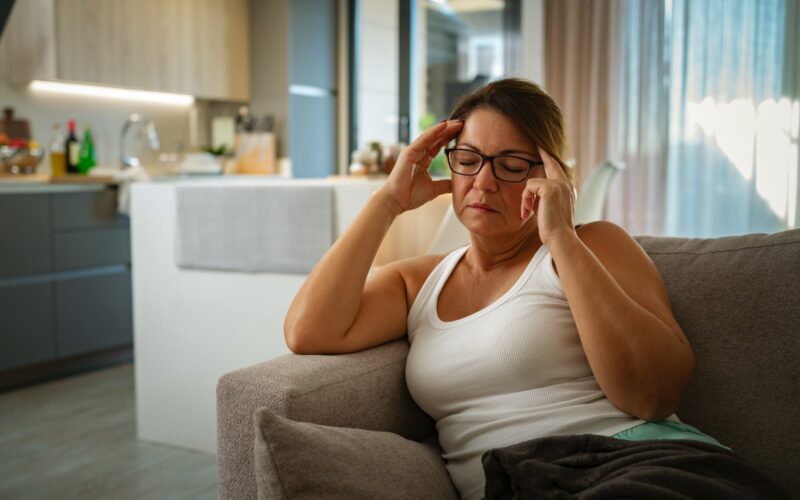 woman sitting on a couch practicing self-massage techniques by pressing her temples, symbolizing stress relief and relaxation at home